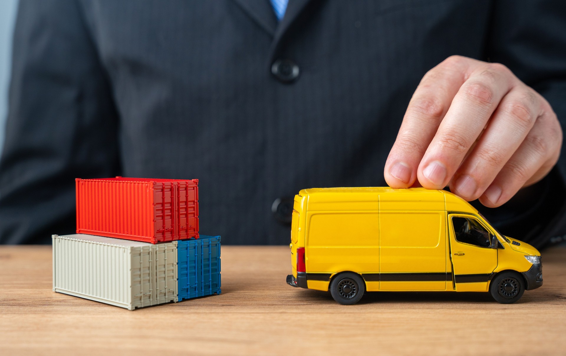 A businessman pushes a delivery van past a stack of shipping containers. The concept of delivery and transportation of goods and parcels to the end customer. Logistics and speed.